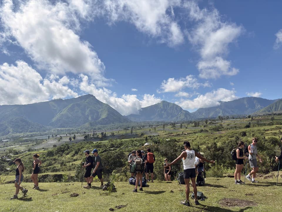 Gruppe beim Wandern über eine grüne Hochebene, dahinter Berge
